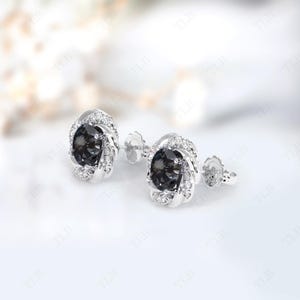 Peut inclure: Une paire de boucles d'oreilles en argent avec une pierre pr&eacute;cieuse noire entour&eacute;e de petites pierres blanches.