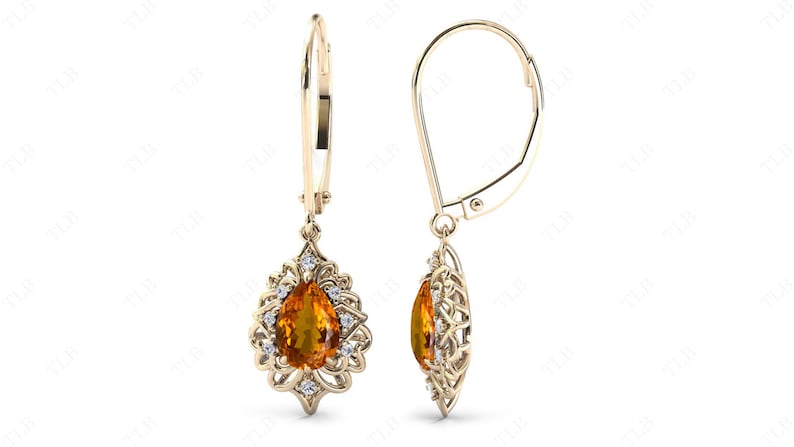 Op de afbeelding: Een paar gouden oorhangers met een peervormige oranje edelsteen omringd door kleinere witte edelstenen. De oorbellen hebben een sluiting met een hendel.
