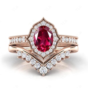 May include: A rose gold engagement ring set with a large oval ruby centre stone surrounded by a halo of small diamonds. The set includes a matching band with diamonds and a chevron-shaped band.