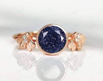 Könnte beinhalten: Ein Ring aus Roségold mit einem blauen Edelstein und zwei Bienen-Akzenten auf jeder Seite. Der Edelstein ist rund und hat eine funkelnde, strukturierte Oberfläche.