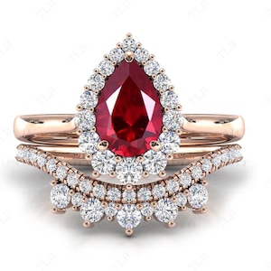 Op de afbeelding: Een peervormige robijn verlovingsring met een halo van kleinere diamanten gezet in roségoud. De ring wordt geleverd met een bijpassende trouwring met een rij diamanten.