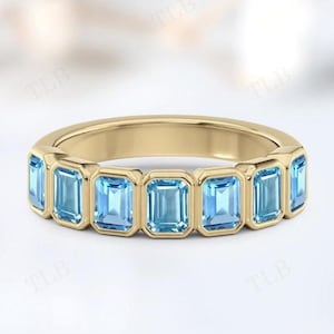 May include: A gold band ring with seven light blue emerald-cut gemstones set in a row.