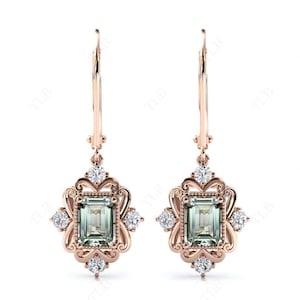 Può includere: Un paio di orecchini pendenti in oro rosa con una pietra preziosa verde quadrata e pietre preziose trasparenti più piccole incastonate in un design a filigrana.