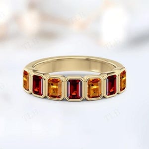 Peut inclure: Une bague en or ornée d'une série de pierres précieuses rectangulaires aux tons rouges, oranges et jaunes. Les pierres sont serties en une bande continue, créant un design vibrant. La bague est un bijou.