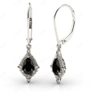 May include: A pair of silver dangle earrings with a pear-shaped black gemstone surrounded by smaller white gemstones. The earrings have a leverback closure.