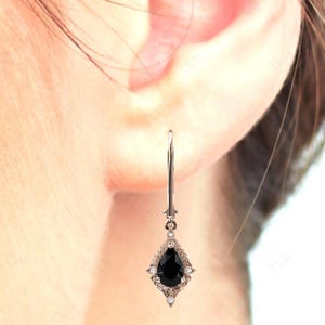 May include: A pair of silver dangle earrings with a pear-shaped black gemstone surrounded by smaller white gemstones.