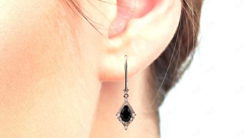 May include: A pair of silver dangle earrings with a pear-shaped black gemstone surrounded by smaller white gemstones.