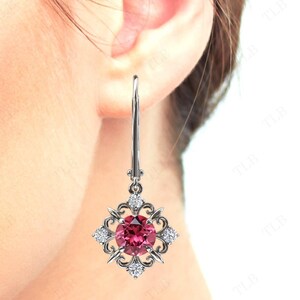 May include: Silver dangle earrings with a pink gemstone surrounded by smaller clear gemstones in a square setting.