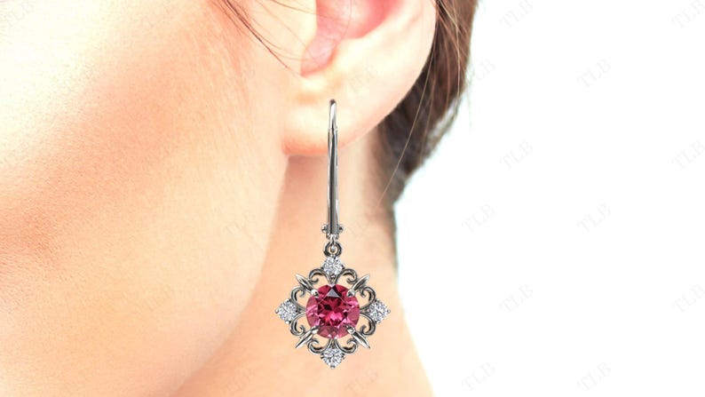 May include: Silver dangle earrings with a pink gemstone surrounded by smaller clear gemstones in a square setting.
