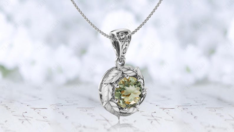 Pu&ograve; includere: Una collana d'argento con un ciondolo di pietra preziosa verde circondato da dettagli a forma di foglie.