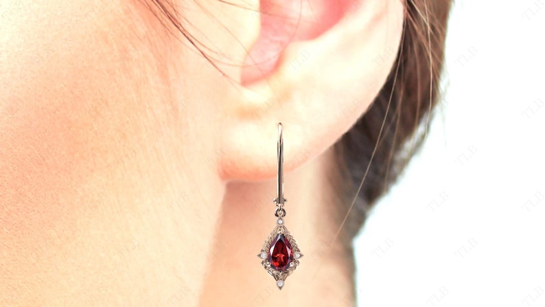May include: A pair of silver dangle earrings with a pear-shaped red gemstone surrounded by smaller white gemstones.