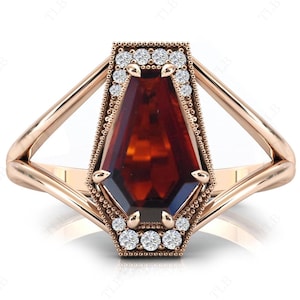 May include: A rose gold ring featuring a large, dark red gemstone set in a geometric, vintage-inspired setting. The gemstone is surrounded by a halo of smaller, clear diamonds.