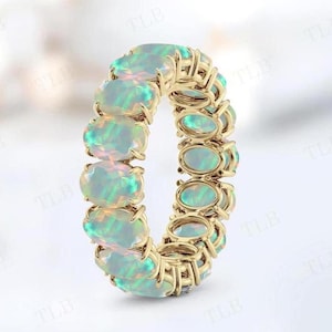 May include: A gold band ring with a row of oval-shaped opal gemstones. The opals are a pale green and white color.