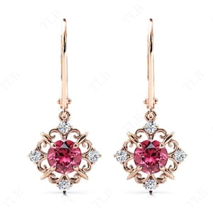 May include: A pair of rose gold dangle earrings with a pink gemstone surrounded by smaller clear gemstones in a filigree design.