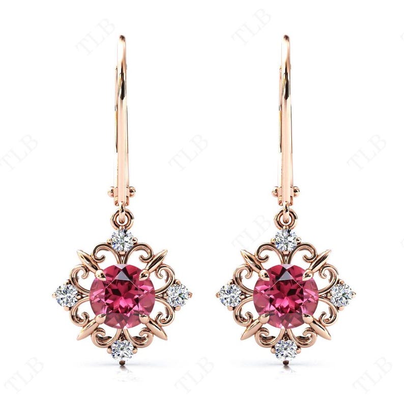 May include: A pair of rose gold dangle earrings with a pink gemstone surrounded by smaller clear gemstones in a filigree design.