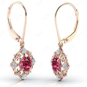 May include: A pair of rose gold dangle earrings with a red gemstone and white gemstones in a floral design.