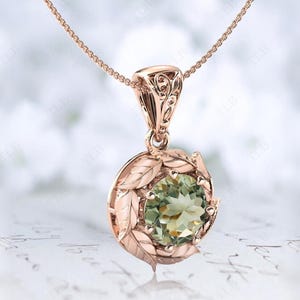 Pu&ograve; includere: Una collana con un ciondolo in oro rosa con una pietra preziosa verde circondata da delicati dettagli a forma di foglie.