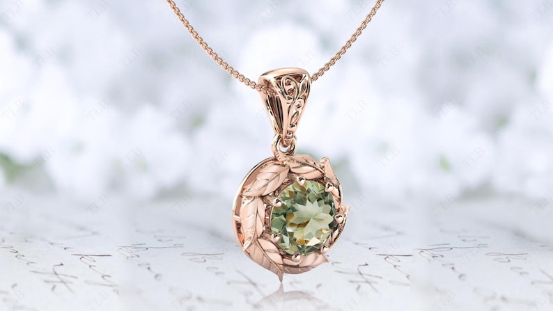 Pu&ograve; includere: Una collana con un ciondolo in oro rosa con una pietra preziosa verde circondata da delicati dettagli a forma di foglie.