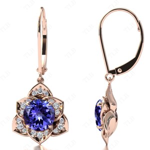 Pu&ograve; includere: Orecchini pendenti in oro rosa con una pietra preziosa blu circondata da pietre bianche pi&ugrave; piccole. Gli orecchini hanno una chiusura a leva.