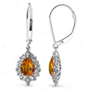 Op de afbeelding: Een paar zilveren oorhangers met een peervormige oranje edelsteen gezet in een filigraan ontwerp.
