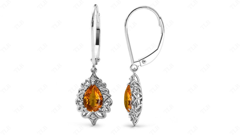 Op de afbeelding: Een paar zilveren oorhangers met een peervormige oranje edelsteen gezet in een filigraan ontwerp.