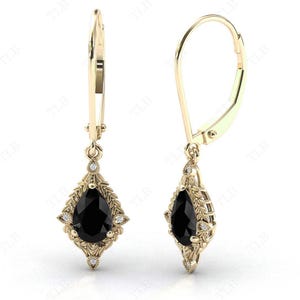 May include: A pair of gold dangle earrings with a pear-shaped black gemstone surrounded by smaller white gemstones.