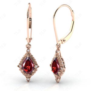 May include: A pair of dangle earrings with a pear-shaped red gemstone surrounded by smaller white gemstones. The earrings are made of gold and have a leverback closure.