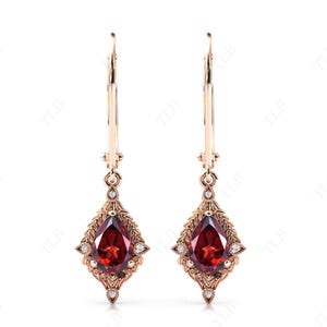 May include: A pair of dangle earrings with a pear-shaped red gemstone and small clear gemstones set in a gold filigree design.