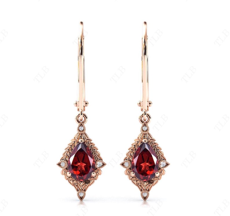 May include: A pair of dangle earrings with a pear-shaped red gemstone and small clear gemstones set in a gold filigree design.