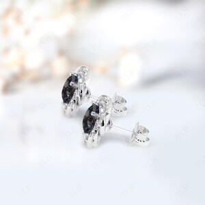 Peut inclure: Une paire de boucles d'oreilles en argent avec une pierre pr&eacute;cieuse noire sertie dans un halo d'argent. Les boucles d'oreilles ont un fermoir &agrave; tige et papillon.