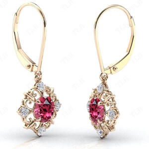 May include: A pair of gold dangle earrings with a red gemstone and small white gemstones in a filigree design.