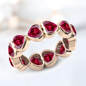 Puede incluir: Un anillo de eternidad de oro rosa con una fila continua de piedras preciosas de rubí en forma de corazón.