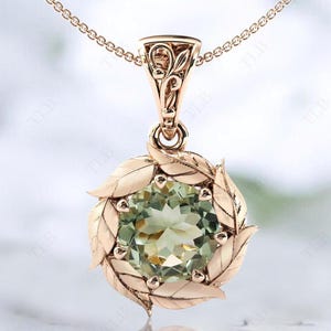 Pu&ograve; includere: Una collana con un ciondolo in oro rosa con una pietra preziosa verde circondata da un delicato design a foglie.