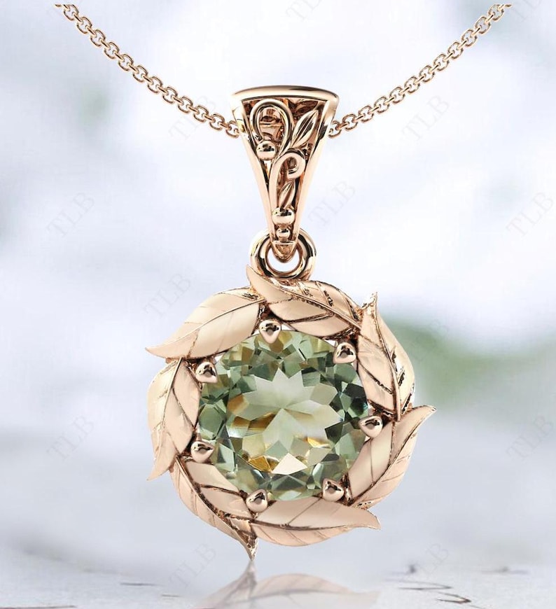 Pu&ograve; includere: Una collana con un ciondolo in oro rosa con una pietra preziosa verde circondata da un delicato design a foglie.