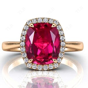 May include: A rose gold ring featuring a large, cushion-cut ruby set within a halo of smaller diamonds.