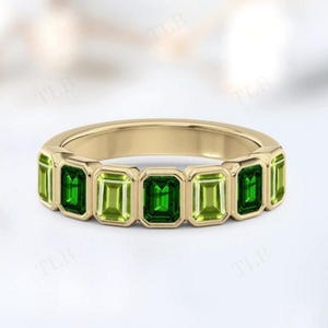 Puede incluir: Un anillo de oro con una serie de piedras preciosas verdes de talla esmeralda. El anillo tiene una banda de oro pulido y tonos alternos de piedras verdes claras y oscuras. Las piedras preciosas están engastadas en un engaste de bisel.