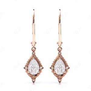 Puede incluir: Un par de pendientes colgantes de oro rosa con piedras preciosas transparentes en forma de pera engastadas en un dise&ntilde;o delicado y ornamentado.