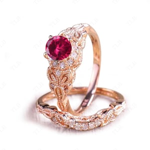 Peut inclure: Une bague de fiançailles d'inspiration vintage avec un gros rubis de forme ovale entouré de petits diamants. La bague est en or rose et présente un délicat motif floral.