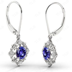 Puede incluir: Un par de pendientes de plata con un colgante de piedra azul rodeado de peque&ntilde;as piedras blancas en un dise&ntilde;o floral.