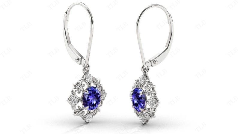 Puede incluir: Un par de pendientes de plata con un colgante de piedra azul rodeado de peque&ntilde;as piedras blancas en un dise&ntilde;o floral.