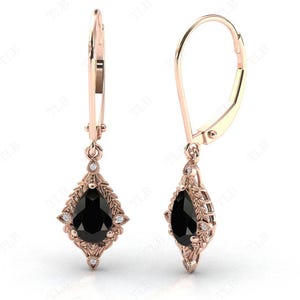 May include: A pair of rose gold dangle earrings with a pear-shaped black gemstone surrounded by smaller white gemstones. The earrings have a leverback closure.