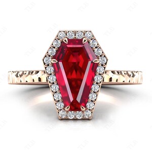 May include: A rose gold ring with a large red ruby gemstone set in a coffin-shaped halo of smaller diamonds.
