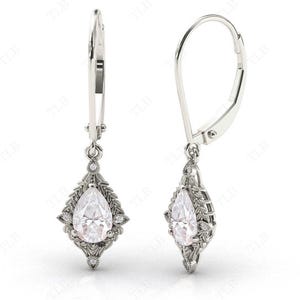 Puede incluir: Un par de pendientes de plata de forma de pera con un dise&ntilde;o floral y piedras transparentes.