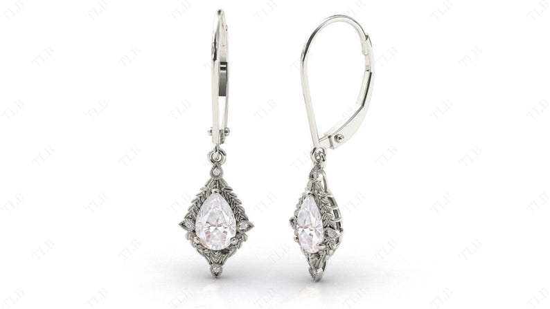 Puede incluir: Un par de pendientes de plata de forma de pera con un dise&ntilde;o floral y piedras transparentes.
