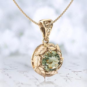 Pu&ograve; includere: Una collana con ciondolo in oro con una pietra preziosa verde circondata da un motivo a foglie.