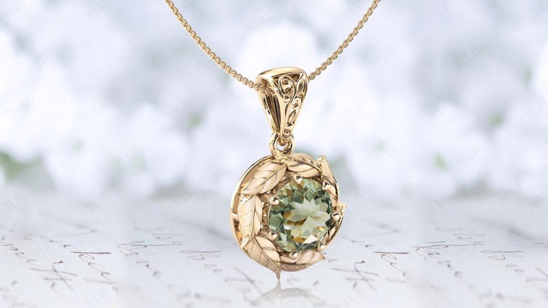 Pu&ograve; includere: Una collana con ciondolo in oro con una pietra preziosa verde circondata da un motivo a foglie.