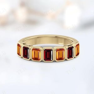 May include: A gold ring featuring a series of rectangular gemstones in alternating shades of orange and red. The gemstones are set in a continuous band, creating a vibrant and eye-catching design. The ring is a piece of jewelry.