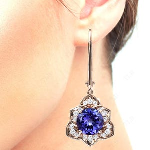 Pu&ograve; includere: Un paio di orecchini pendenti in argento con una grande pietra preziosa blu circondata da piccole pietre bianche a forma di fiore.