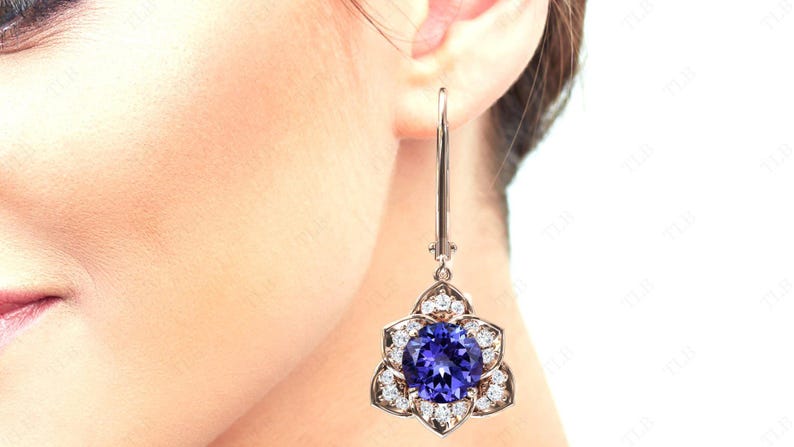Pu&ograve; includere: Un paio di orecchini pendenti in argento con una grande pietra preziosa blu circondata da piccole pietre bianche a forma di fiore.
