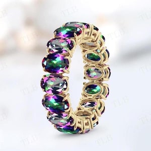 Peut inclure: Une bague en or avec une rangée de pierres précieuses ovales et irisées. Les pierres précieuses sont un mélange de violet, de vert et de bleu.